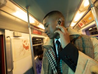 Homme dans le métro choisissant son niveau de réduction de bruit en appuyant deux fois sur l’écouteur Bose QuietComfort II gauche