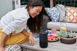 Femme assise à l’extérieur écoutant de musique sur une enceinte portable intelligente Bose