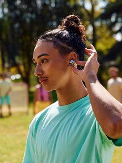 Jeune homme écoutant de la musique, utilisant les commandes tactiles des écouteurs oreilles libres Bose Ultra tout en jouant au foot