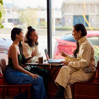 Eine Gruppe, die Bose Ultra Open Earbuds trägt, in einem Café bei der Arbeit an einem Gemeinschaftsprojekt