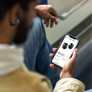 Homme utilisant l’application Bose sur son smartphone pour contrôler ses écouteurs oreilles libres Bose Ultra.