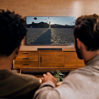 Groupe d’amis regardant la télévision, avec une barre de son intelligente Bose sur une console TV.