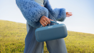 Young woman carrying a Bose SoundLink Max Portable Speaker through a field