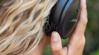 Woman pressing the Action button on the Bose QuietComfort 45 Headphones to toggle between Quiet Mode (noise cancelling) and Aware Mode