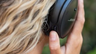 امرأة تضغط على زر Action في سماعات Bose QuietComfort 45 للتبديل بين الوضع الهادئ (إلغاء الضوضاء) ووضع Aware