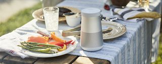 Soundlink Revolve+ Ii Bluetooth Speaker On A Table At An Outdoor Barbecue