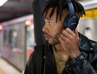 Man wearing Bose QuietComfort 45 headphones in a subway station using the Action button
