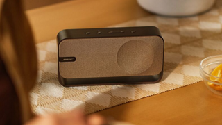 Egy meleg fa színű Bose SoundLink Home Bluetooth-hangsugárzó egy asztalon.