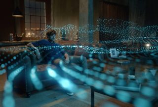 Man in a living room watching TV with sound waves radiating from the speaker system showing the effects of Dolby Atmos.