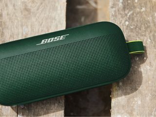 Enceinte Bluetooth SoundLink Flex en vert cyprès par terre avec de l’eau et de la poussière dessus