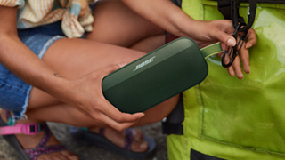Woman attaching a Cypress Green SoundLink Flex Bluetooth Speaker to her backpack